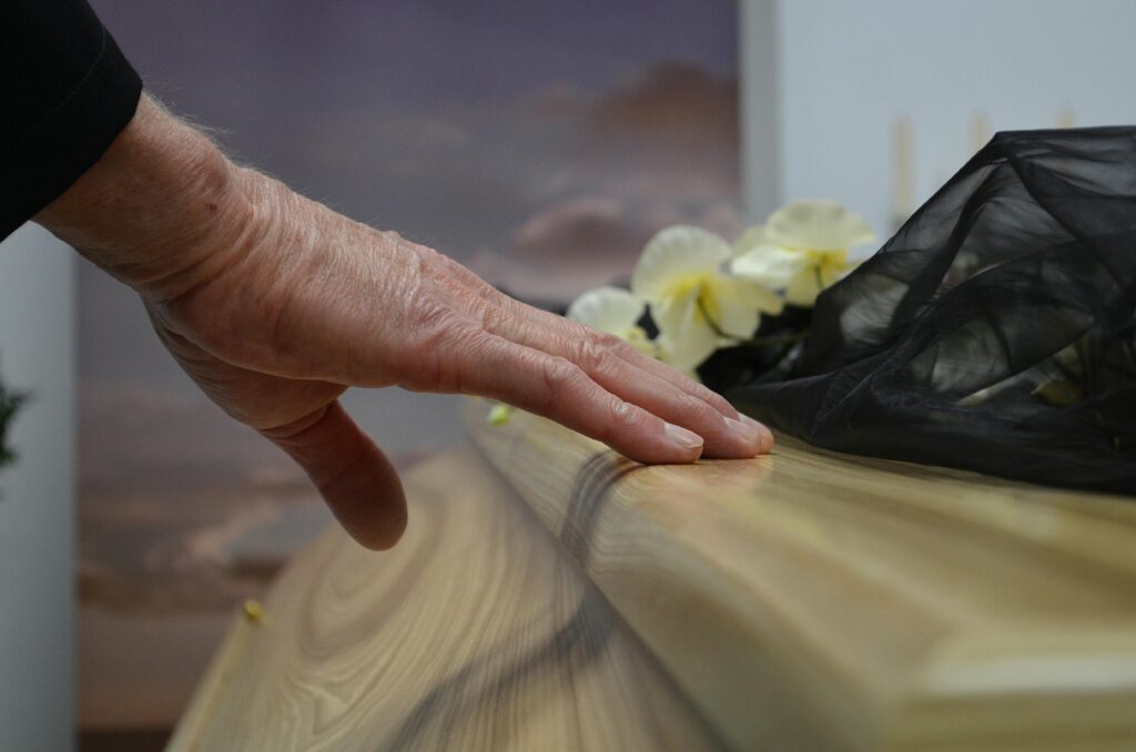 A touching moment of grief as a hand rests on a coffin, symbolizing loss and mourning.